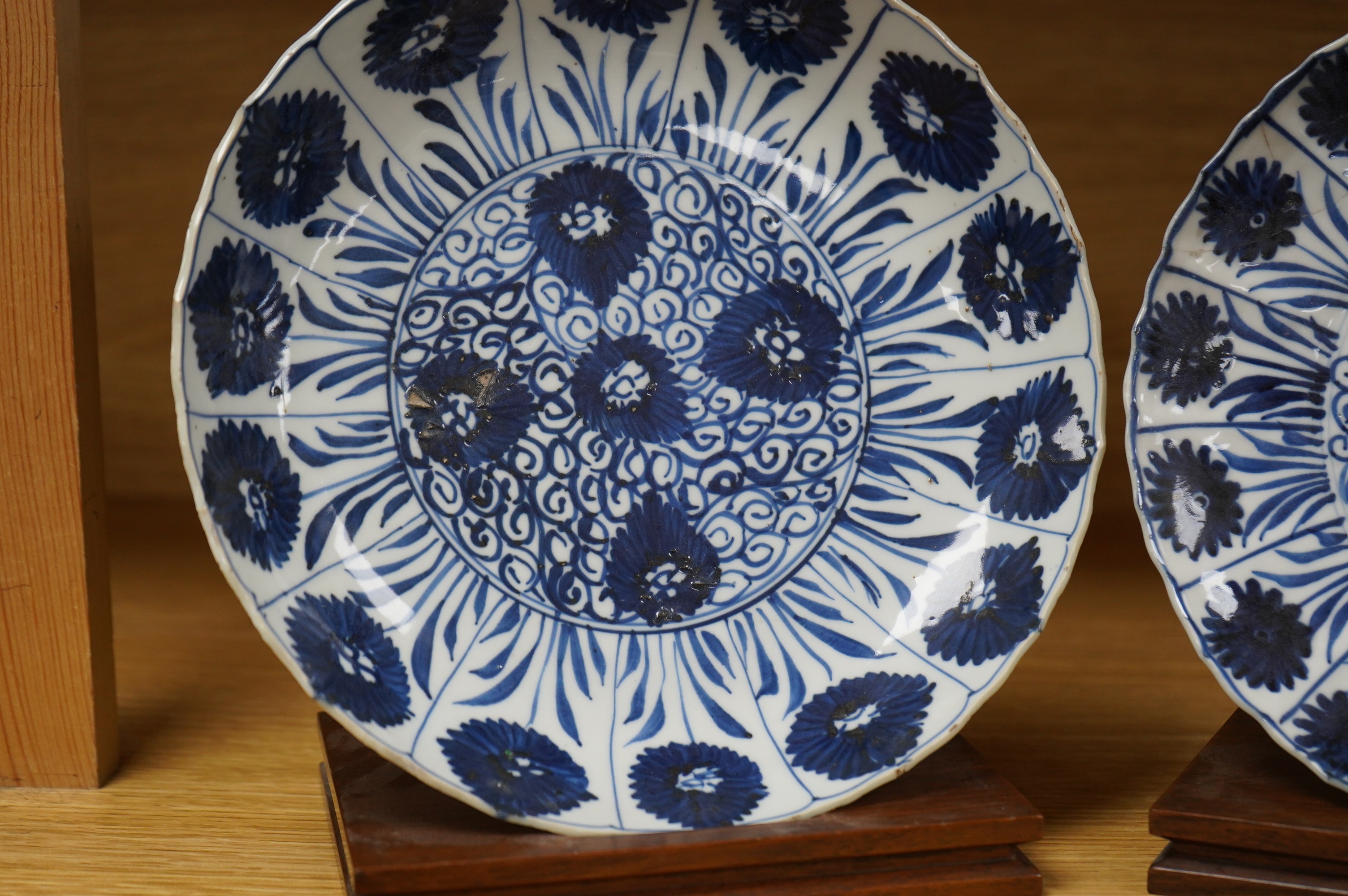 Two Chinese blue and white ‘astor’ plates, Kangxi period, with hardwood stands, largest 22cm diameter. Condition - poor to fair